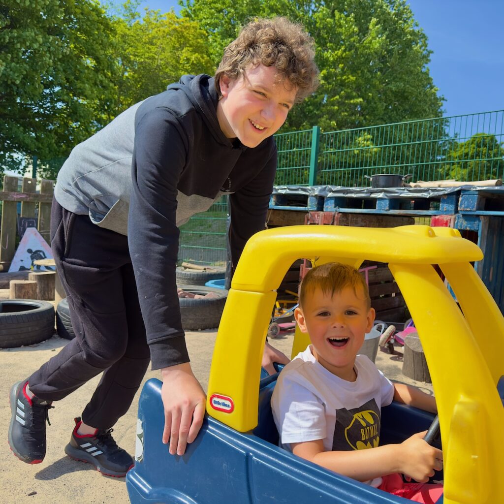 Young person pushing a child in yellow toy car